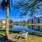 a chair on a lawn by a pond with trees and a house in the background